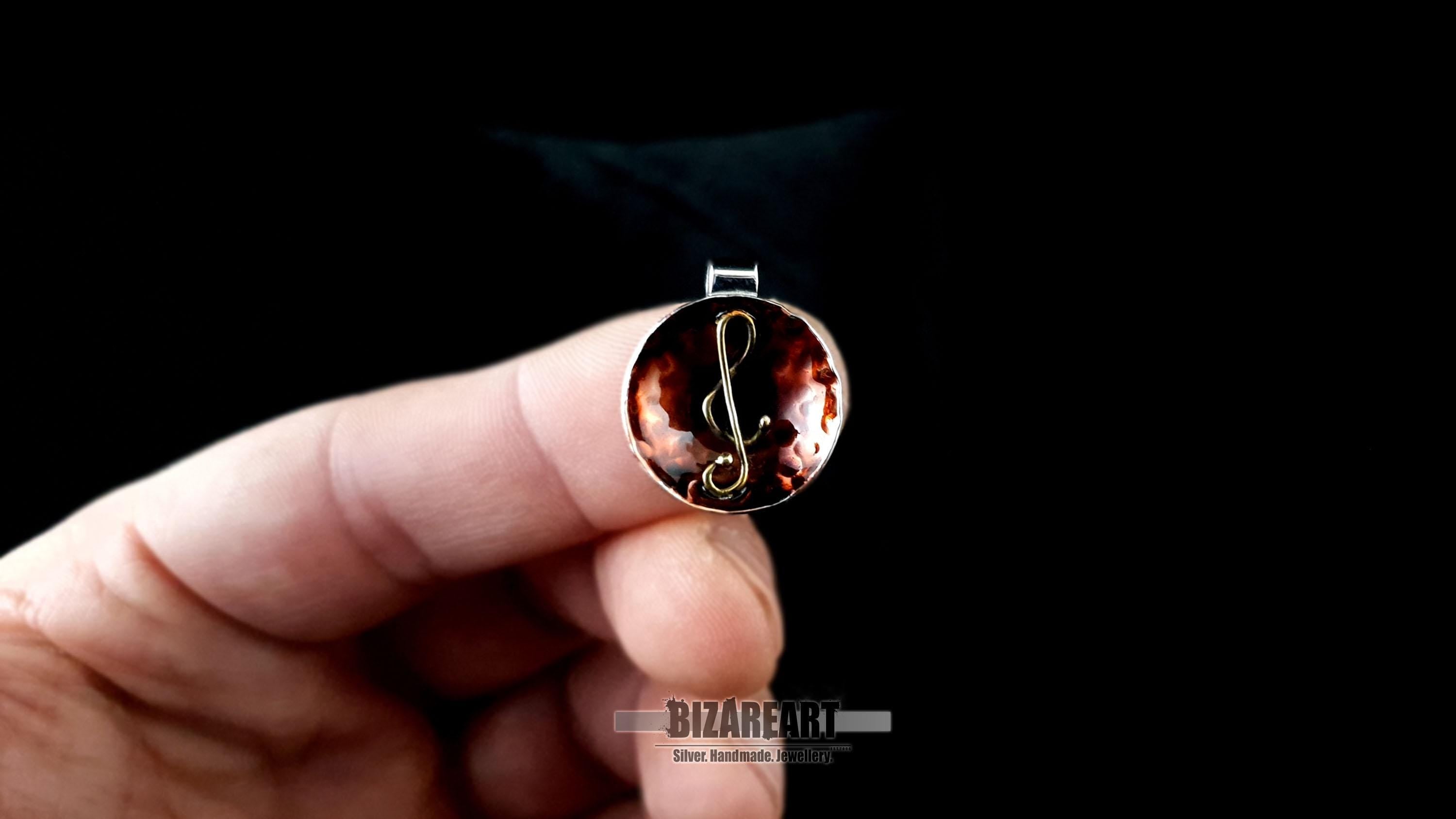 A person’s hand holding the pendant to demonstrate its 2cm scale, emphasizing the intricate gold-plated G-clef detail.