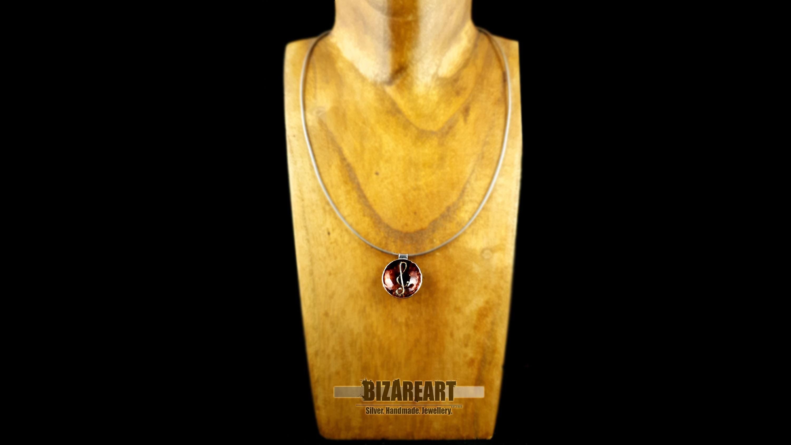 A centered view of the pendant on a black textured surface, focusing on the high-shine rhodium finish and mixed metal contrast.