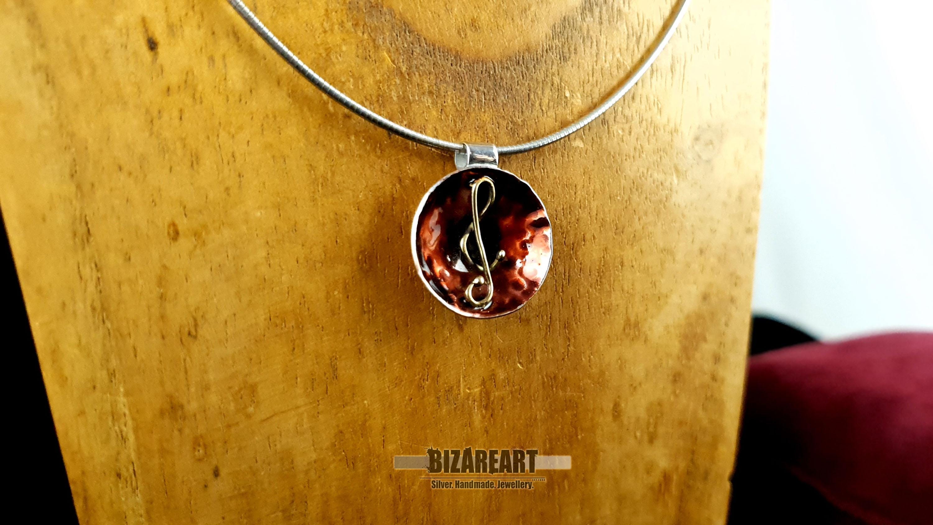 A medium-distance shot of the pendant hanging from a silver chain on a wooden display torso, showing how it sits when worn.