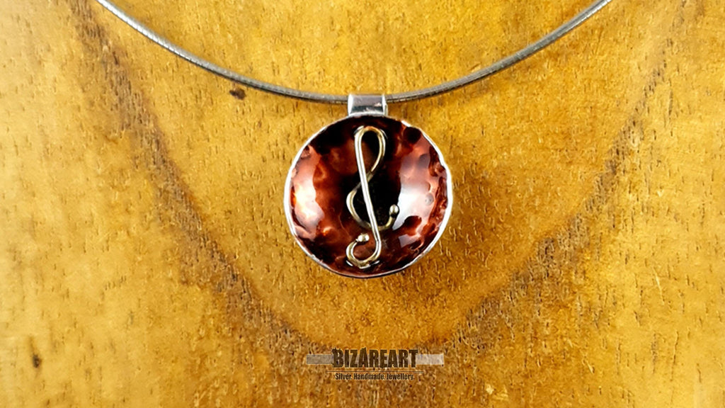 A close-up of the pendant worn on a sleek silver neck wire, displayed against a rustic wooden jewelry bust.
