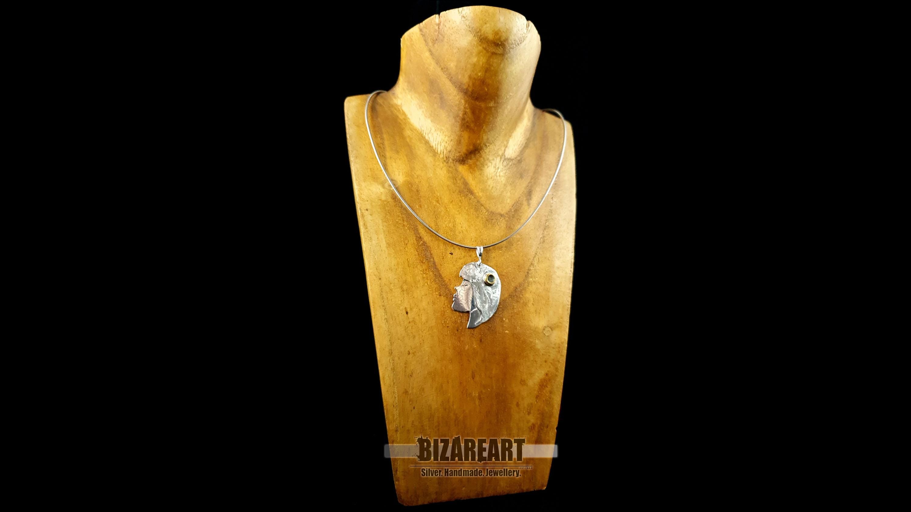 The silver portrait pendant displayed on a delicate silver chain around a wooden jewelry bust to show scale and length.
