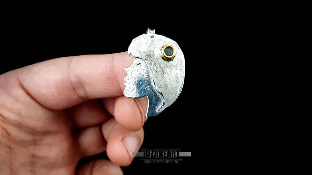A person holding the silver pendant between their fingers, providing a clear reference for the physical size and scale of the piece.