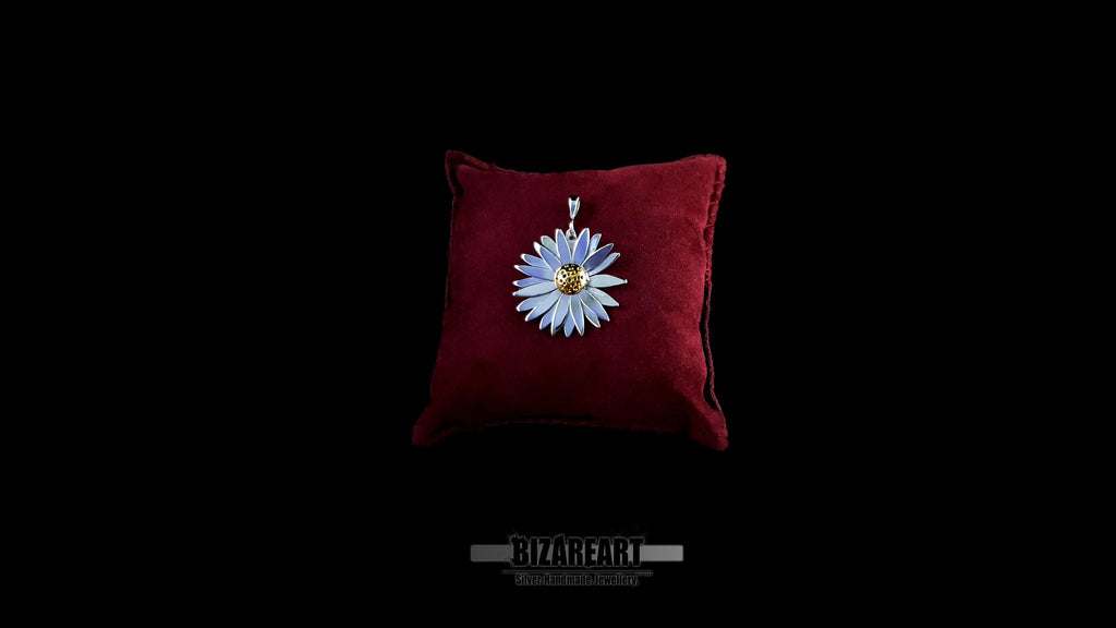 Front view of a handcrafted sterling silver daisy pendant with a gold center, displayed on a plush dark red velvet cushion against a black background.