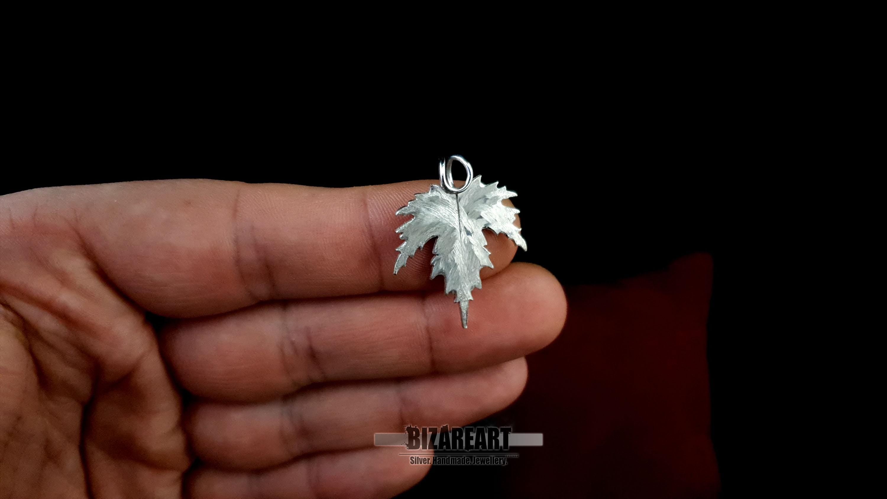 Profile view of the silver leaf being held, showing the depth of the metal carvings and the high-shine rhodium finish.