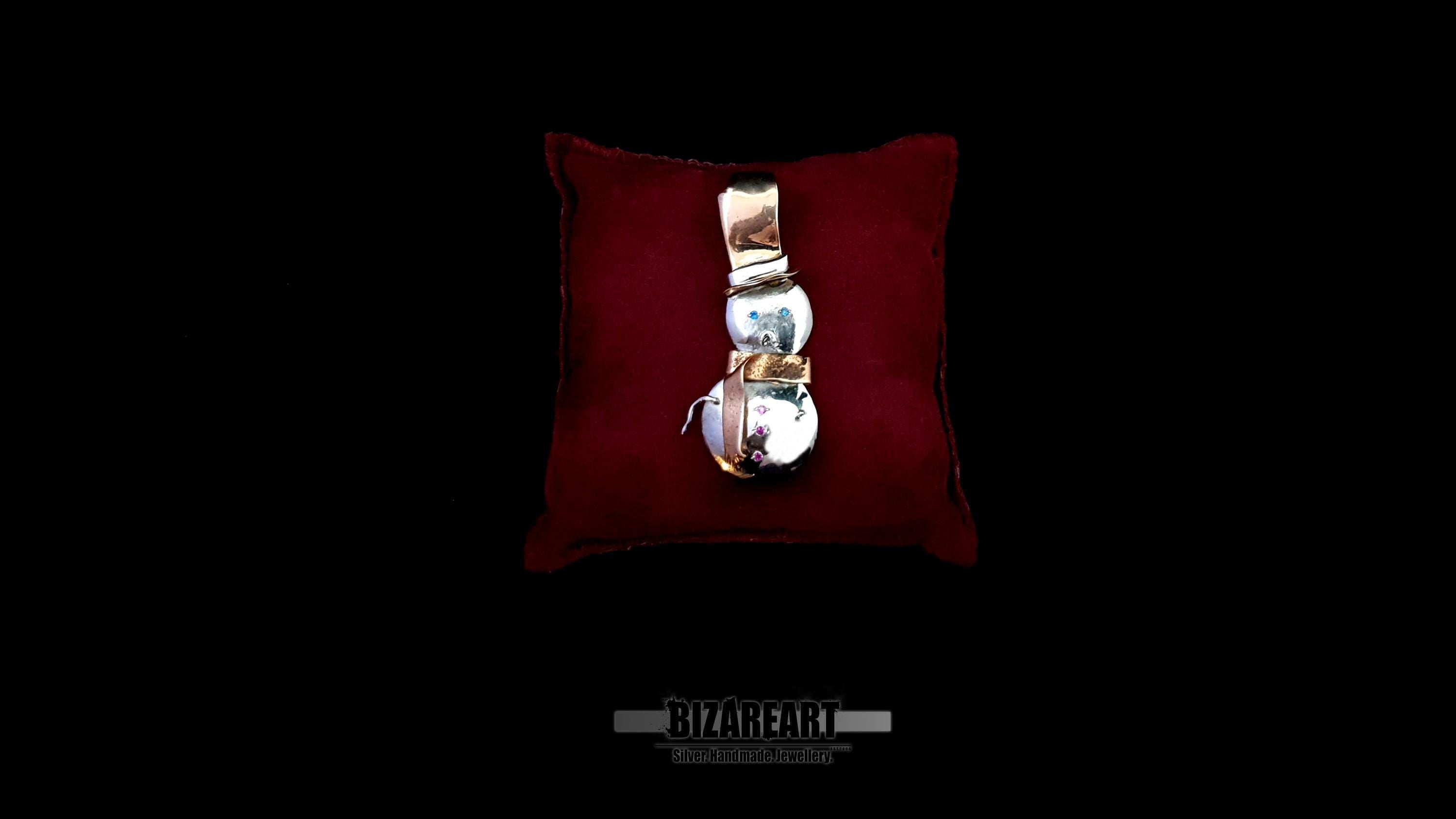 Front view of the BizarreArt handcrafted sterling silver snowman pendant with rose gold accents, resting on a plush red velvet display cushion.