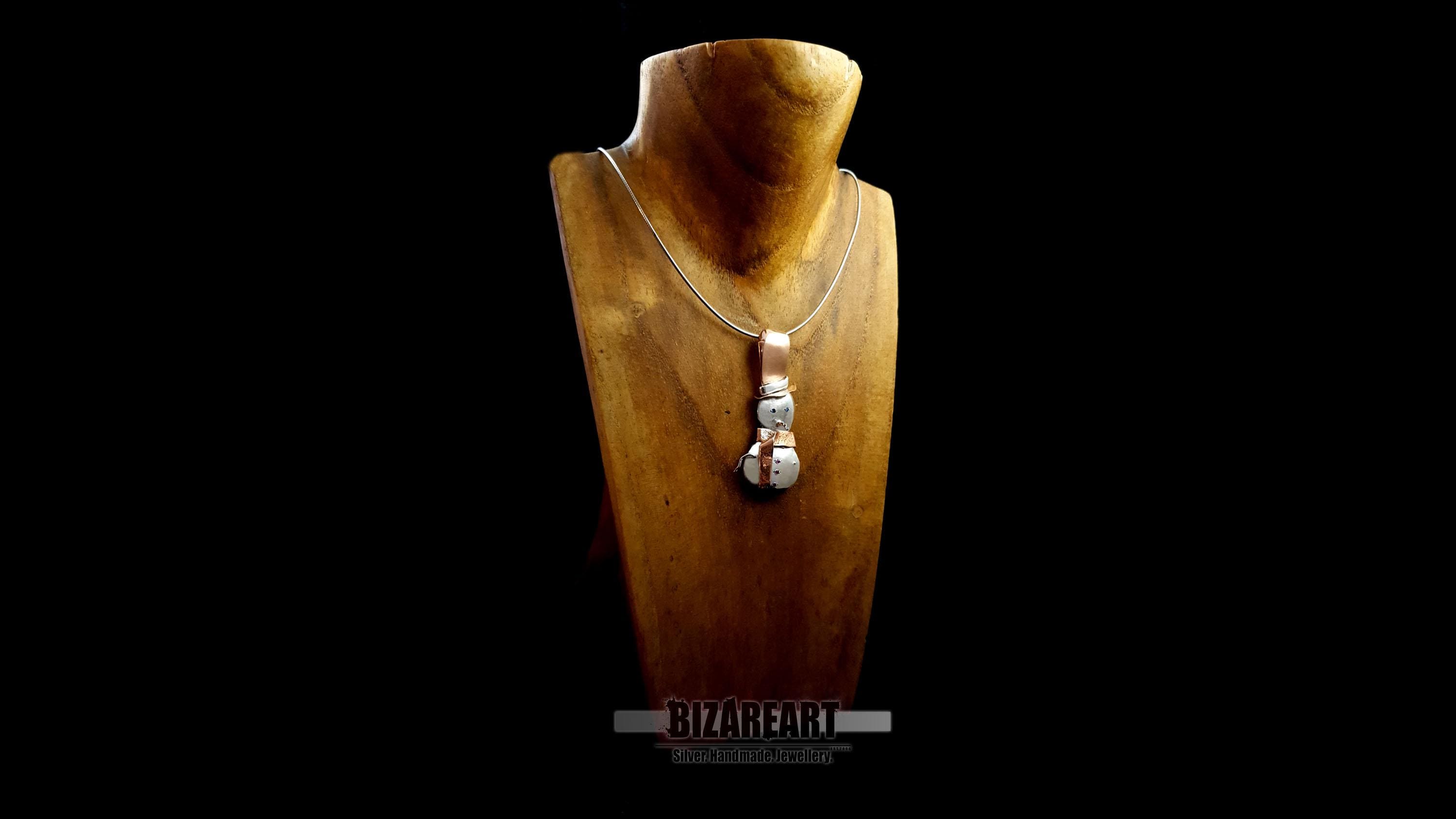 he BizarreArt snowman pendant styled on a silver chain over a wooden jewelry bust, demonstrating how the hidden bail allows it to sit flat.
