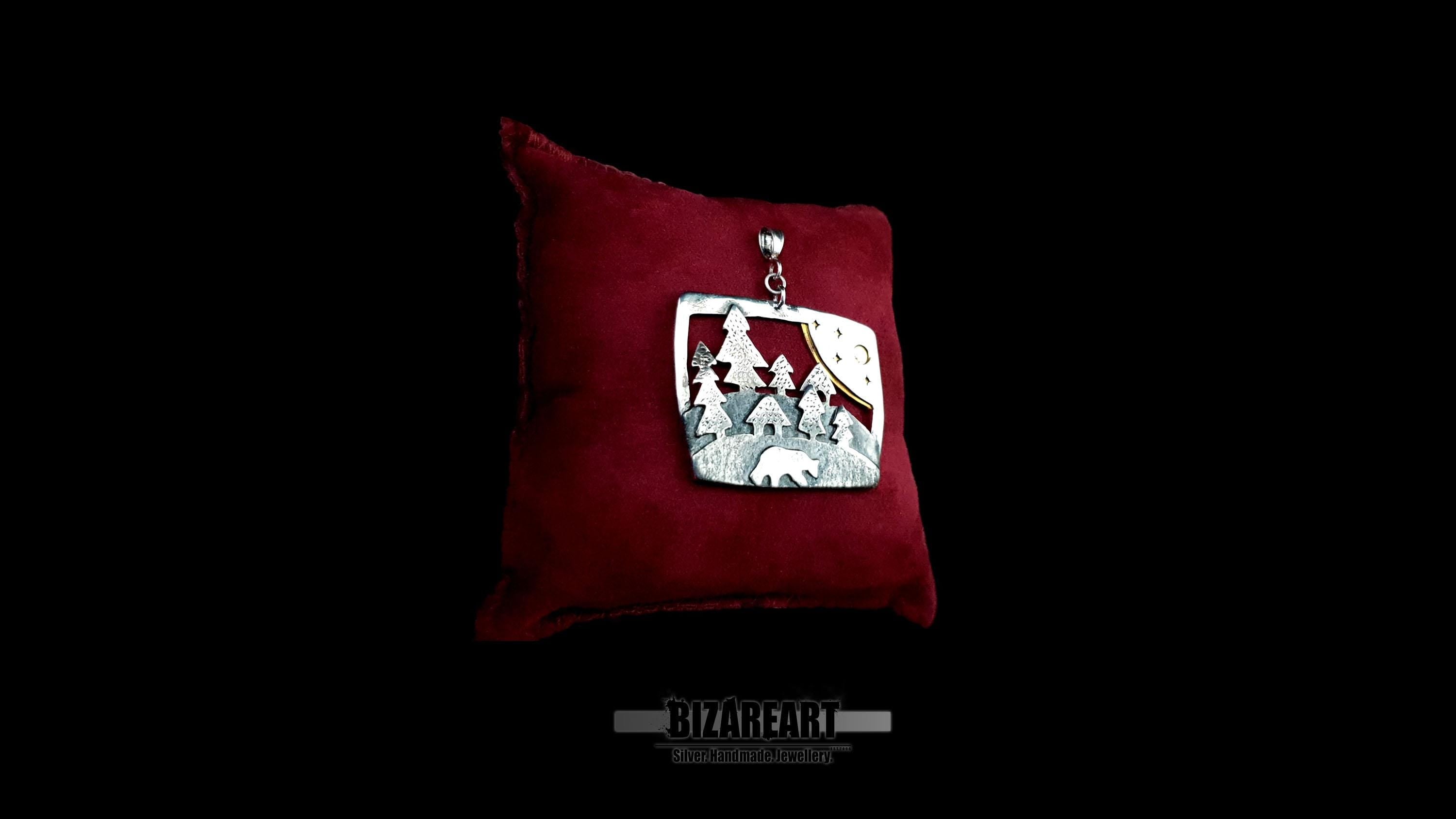 Side perspective view of the 3D multi-layered silver wilderness pendant on a small dark red display cushion, highlighting its substantial thickness.