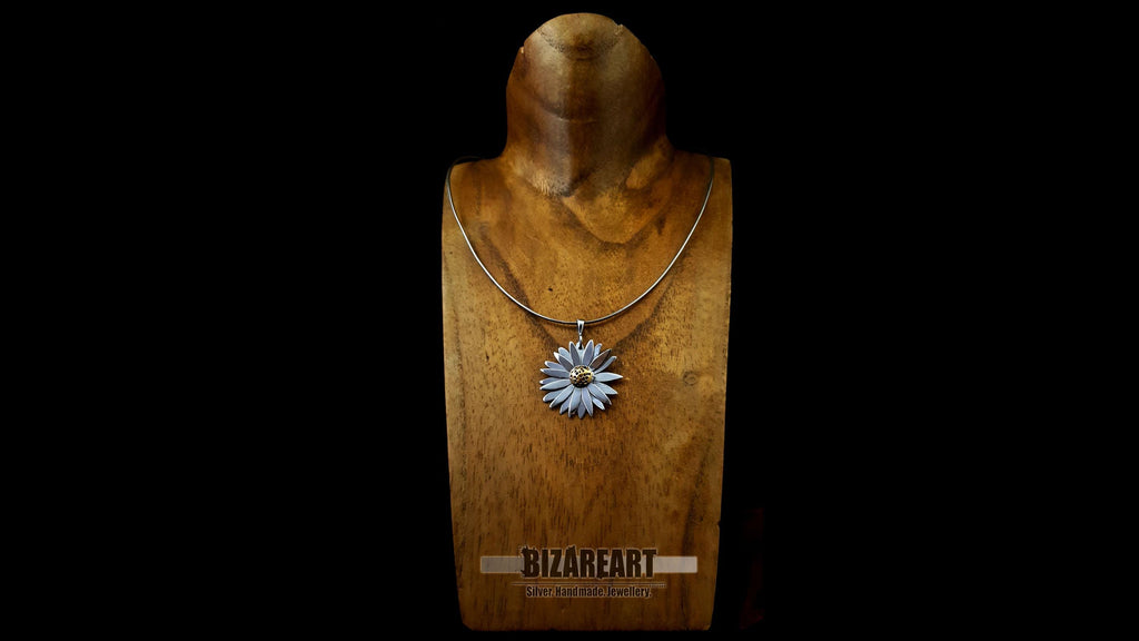 Front view of a handcrafted sterling silver daisy pendant with a gold center, displayed on a plush dark red velvet cushion against a black background.