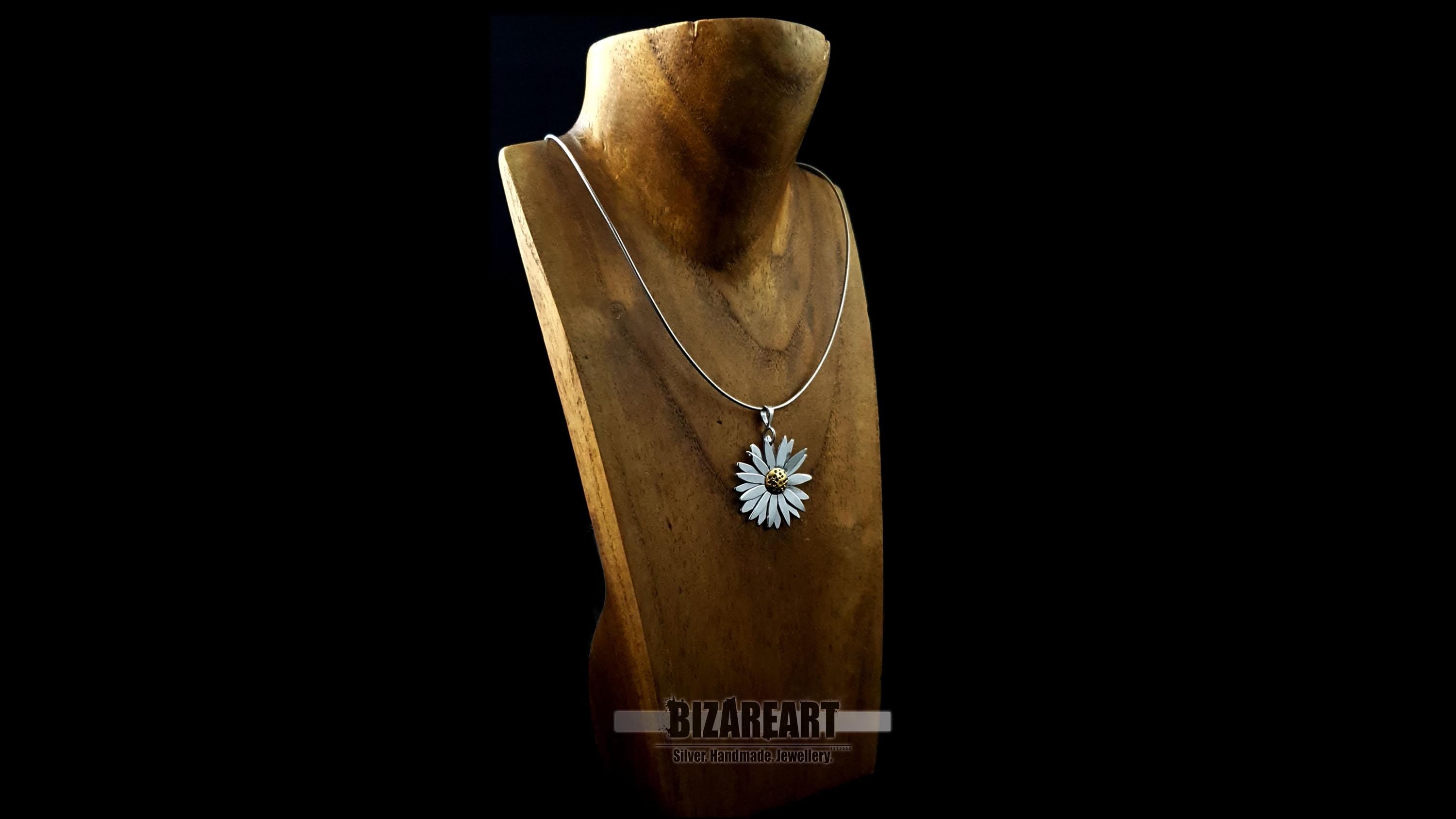 Side profile view of the daisy pendant on a wooden bust, highlighting the architectural double-layer petal design and silver chain.