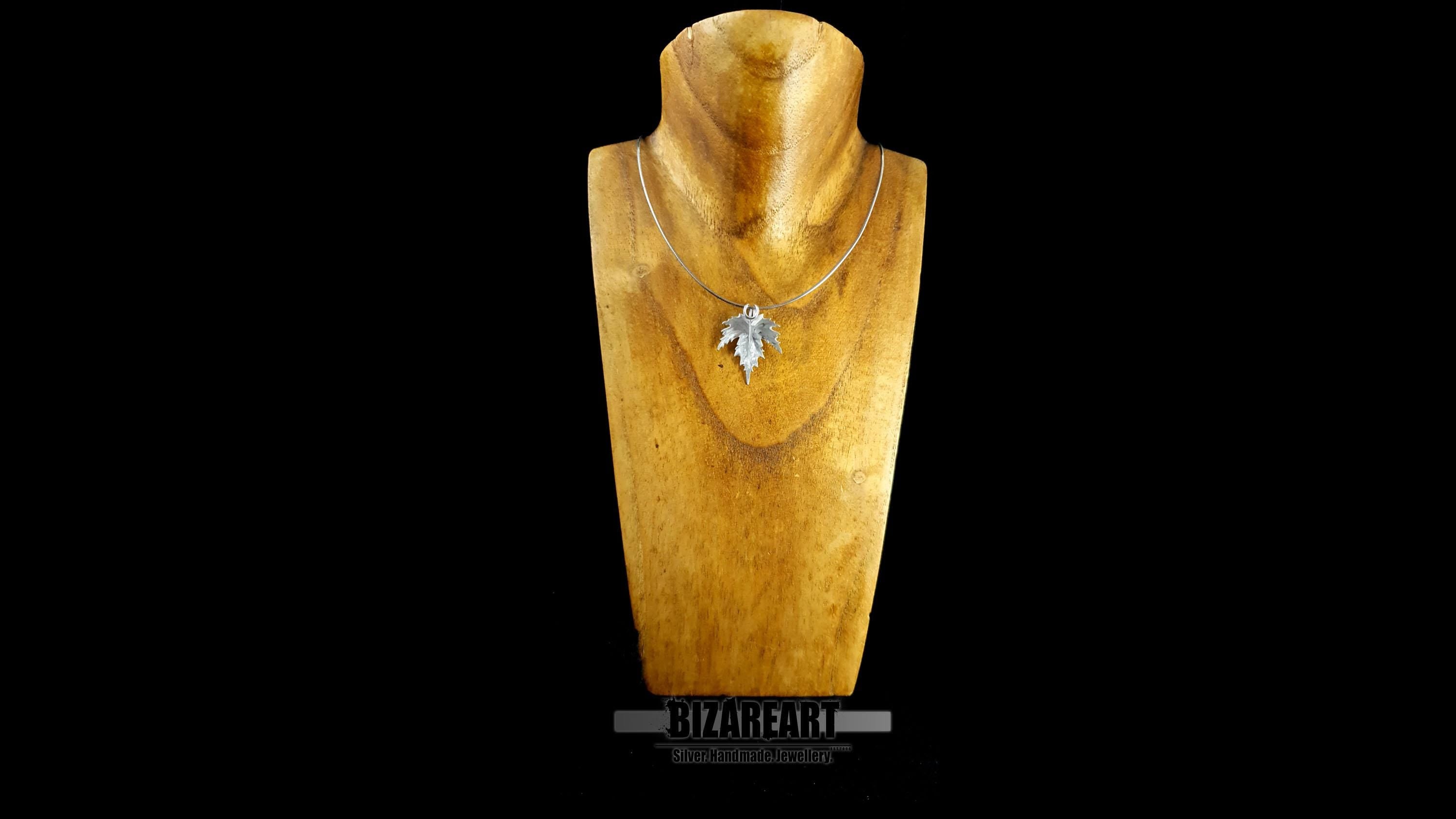The silver leaf pendant displayed on a wooden jewelry bust to show how it sits flush against the chest when worn.