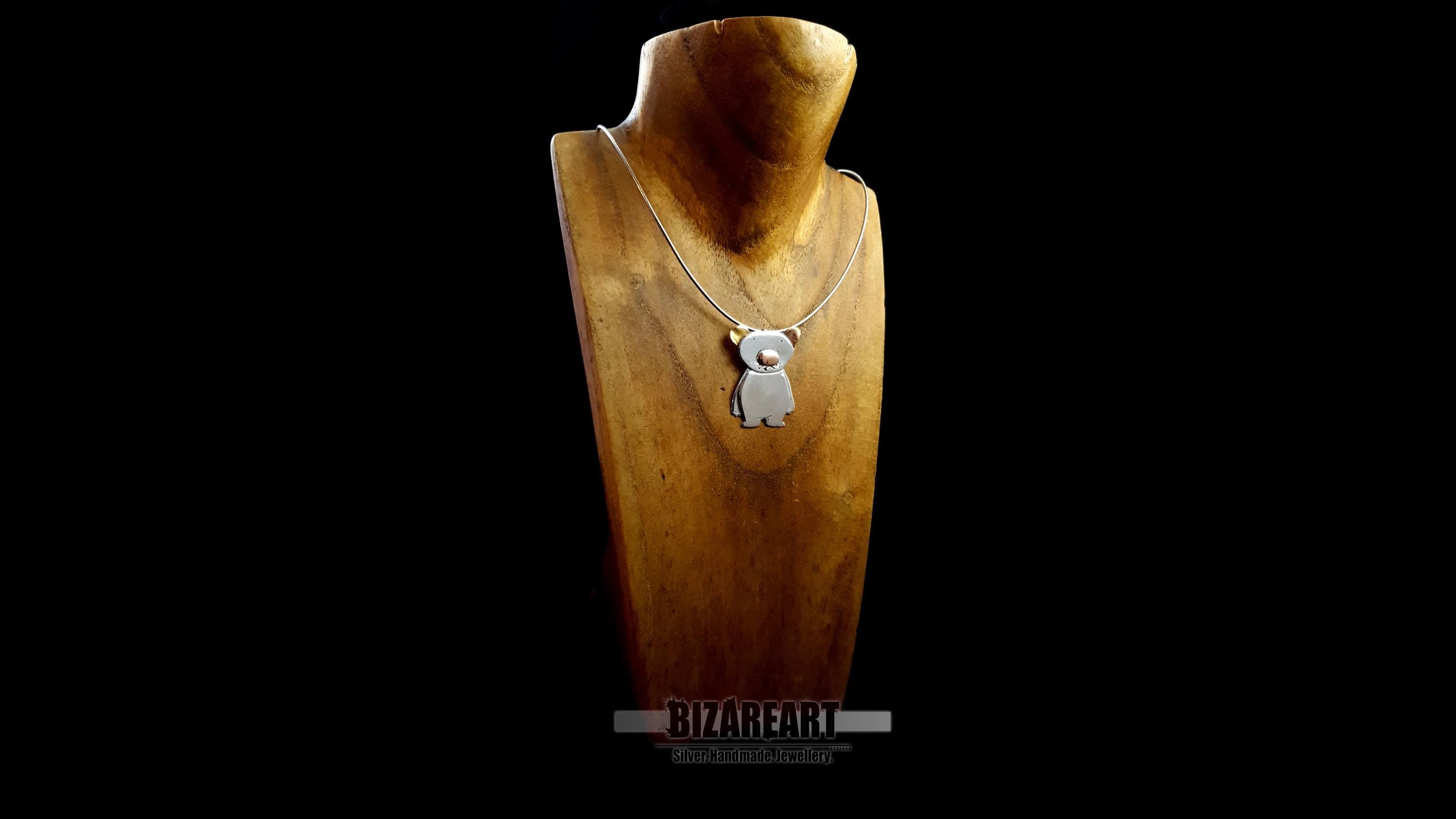 The silver bear pendant displayed on a silver chain, draped over a wooden jewelry bust. This view shows how the pendant hangs and provides a clear sense of its 3.8 cm scale against a torso-shaped display.

