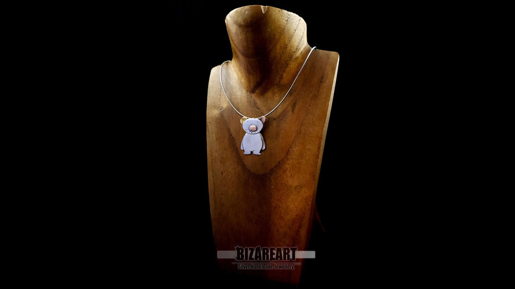 A slightly angled view of the bear pendant on a jewelry bust, showcasing the hand-worked swirl texture on the silver surface and how the rhodium plating catches the light.
