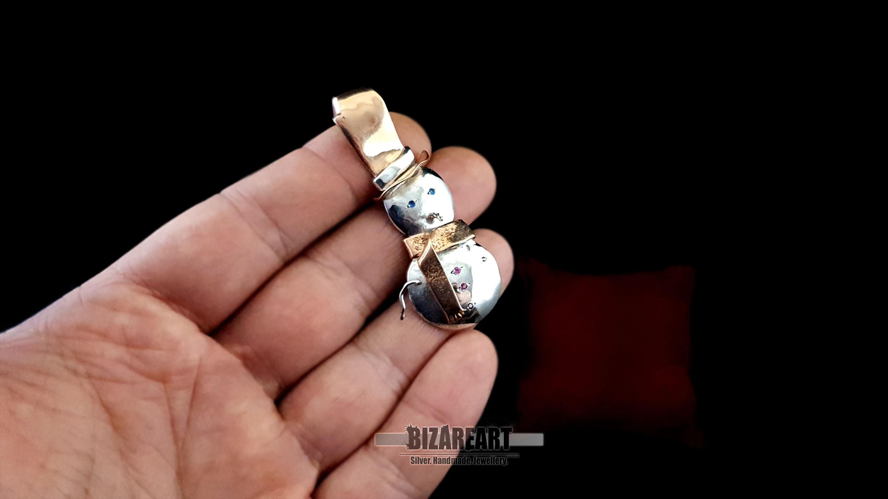 A hand holding the snowman pendant to demonstrate its scale, showing the 6cm height and substantial 10g artisan build.