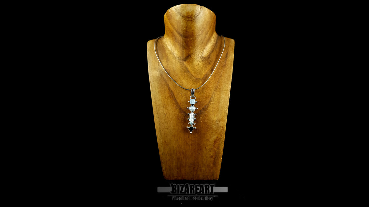 A front view of the Celestial Quad Pendant, handcrafted from sterling silver and featuring a column of moonstone, pearl, and garnet gemstones, worn on a delicate chain around the neck of a neutral-toned wooden display bust against a black background.