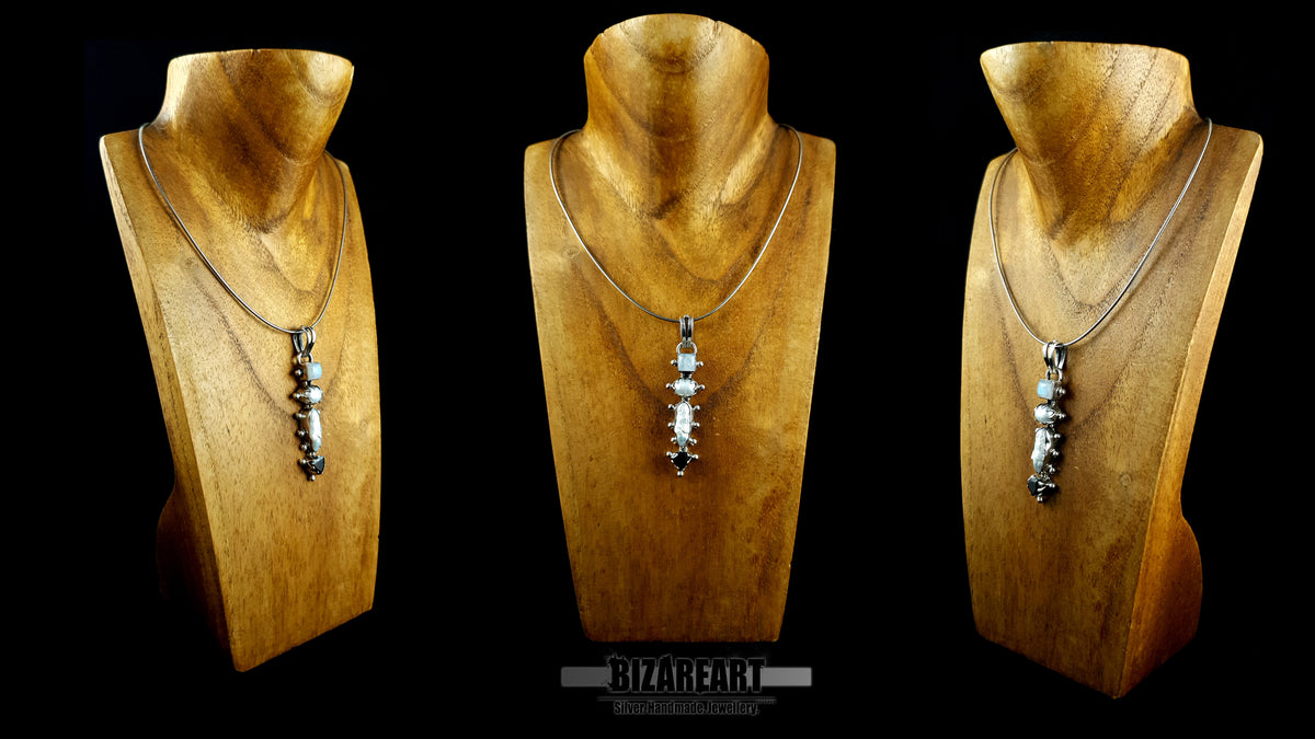 Three varied front views of the artisanal sterling silver quad pendant (moonstone, pearl, garnet), each mounted on a unique wooden display stand to showcase its presence from different angles against a black background.