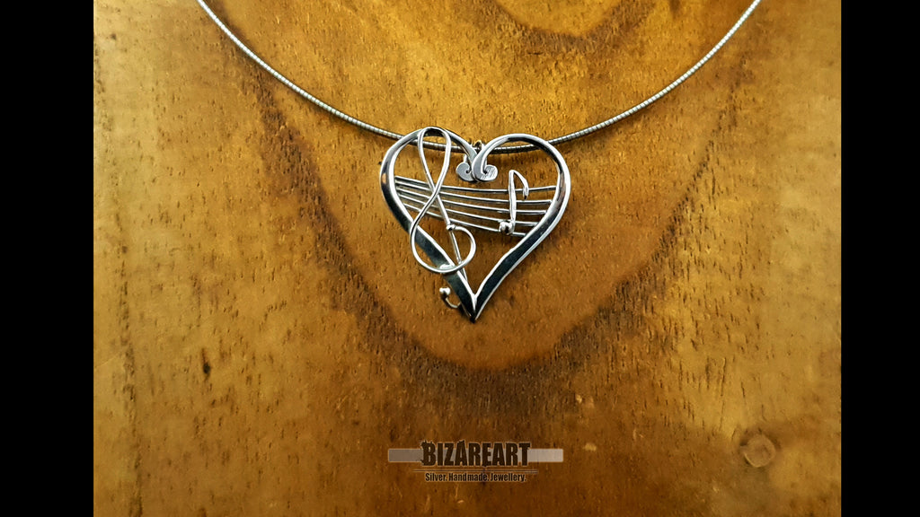 Close-up of the silver heart pendant on a delicate chain, displayed against a rustic, warm-toned wooden backdrop to showcase the scale and high-luster reflection.