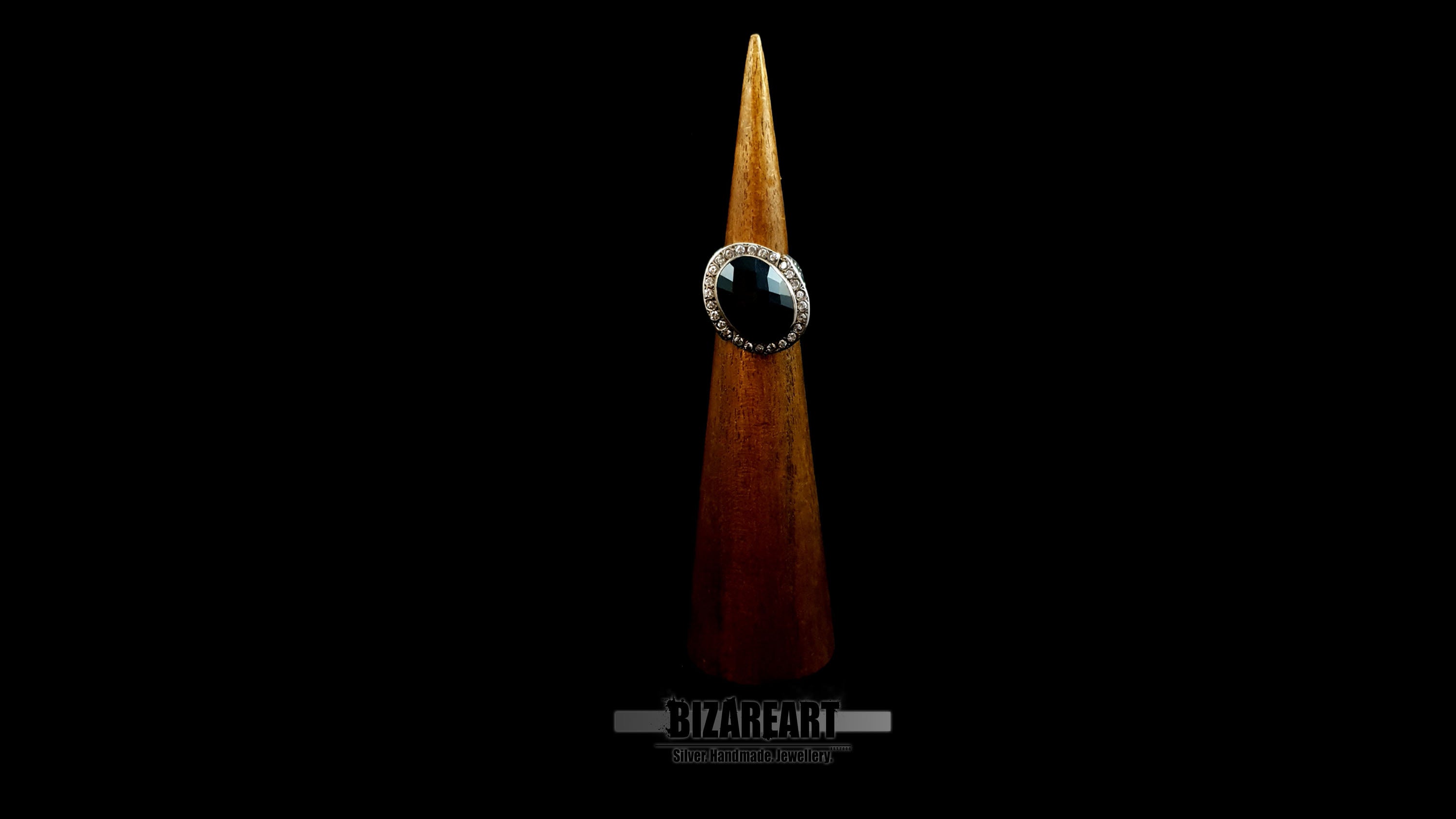 Frontal view of the faceted onyx ring displayed on a wooden jewelry cone, emphasizing the scale and masculine sculptural aesthetic.
