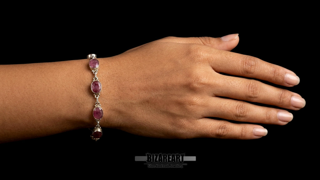 Close-up on-model shot of a woman's wrist wearing the handmade sterling silver link bracelet with six raw oval rubies, presented against a solid black studio background.