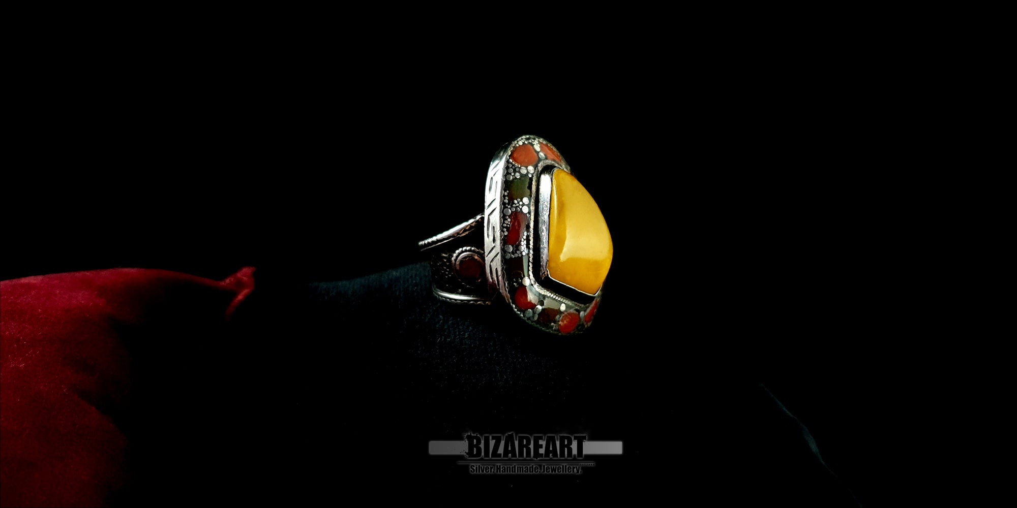 Angled close-up of a handcrafted men's or women's silver ring with a smooth amber gemstone and detailed silver craftsmanship.