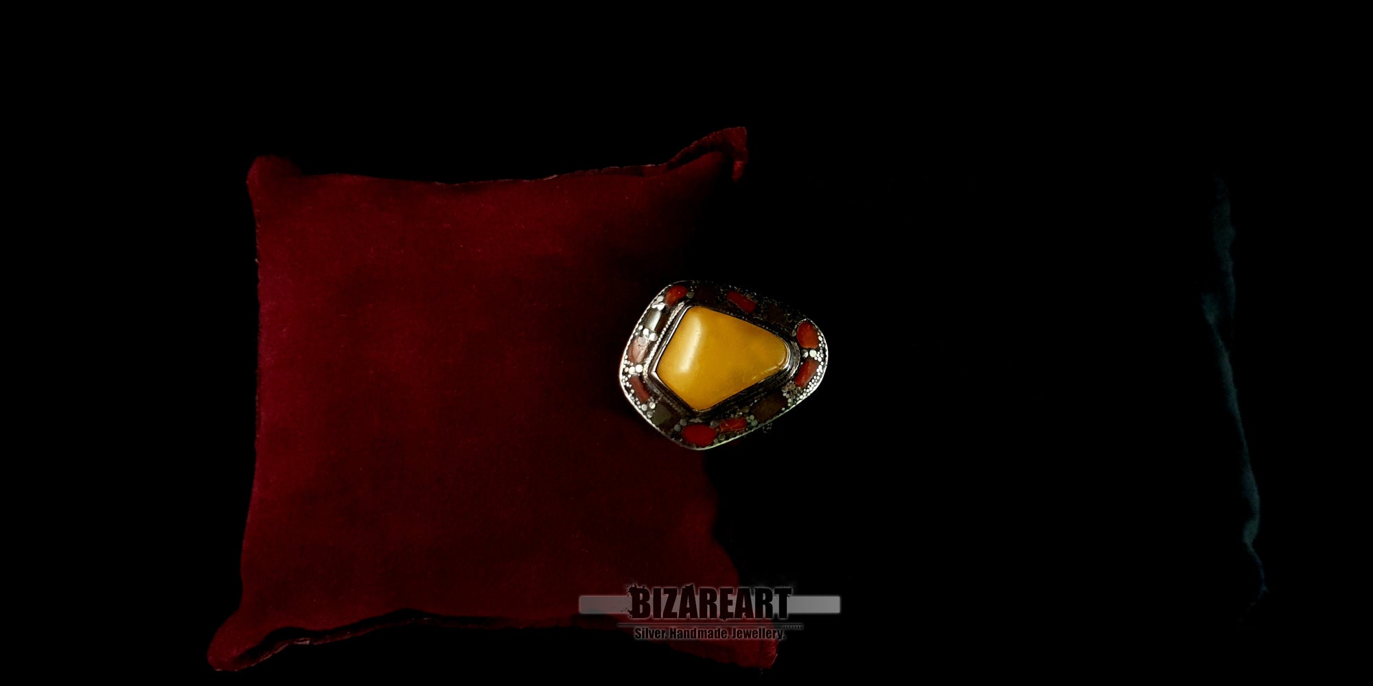 andmade silver statement ring featuring natural amber and red coral gemstones displayed on a luxury red cushion.
