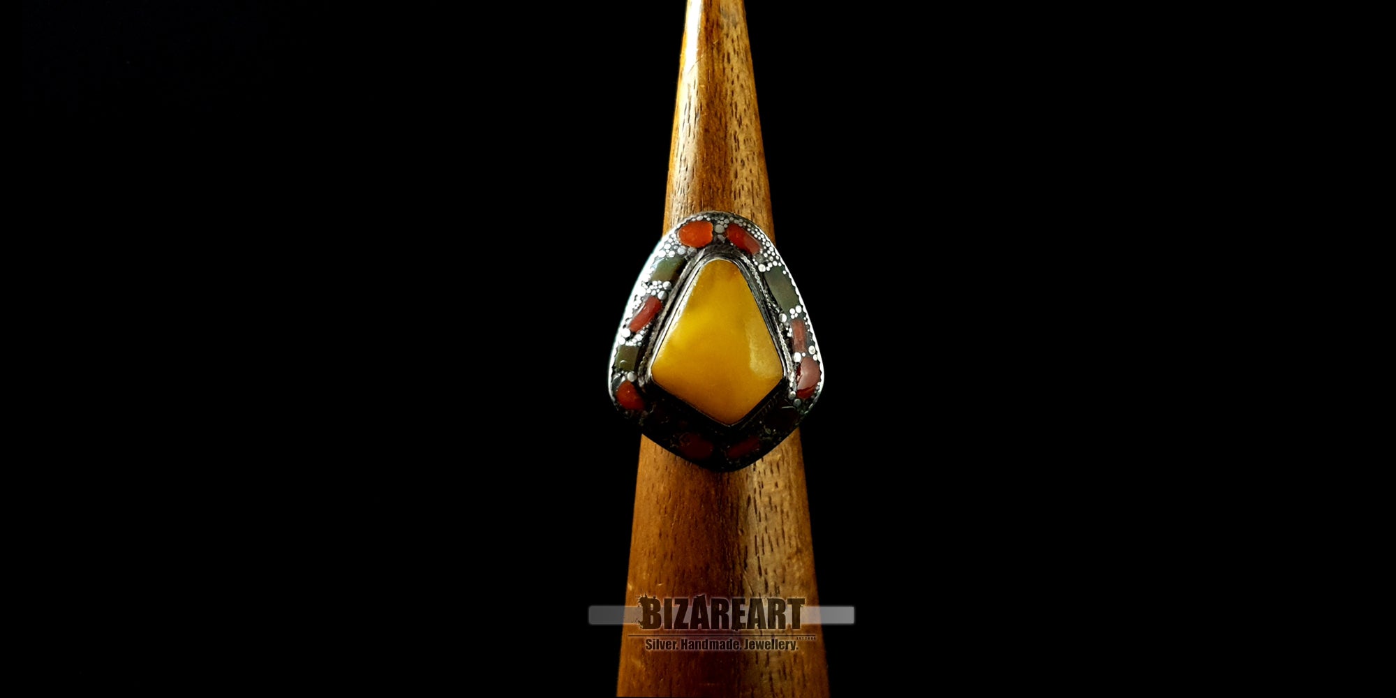 Front view of a thick silver artisan ring showcasing a vibrant yellow amber centerpiece on a wooden jewelry display cone.