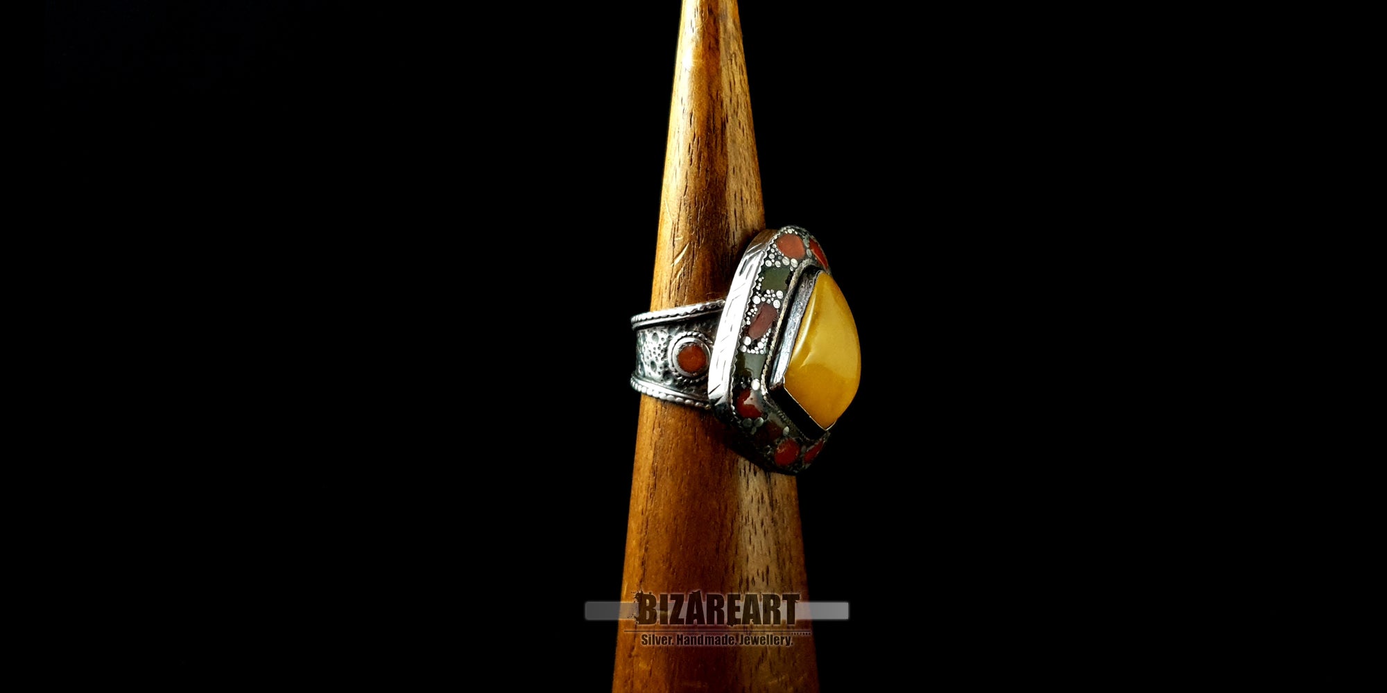 Side profile view of the engraved solid silver band and raised amber setting on a wooden display stand.