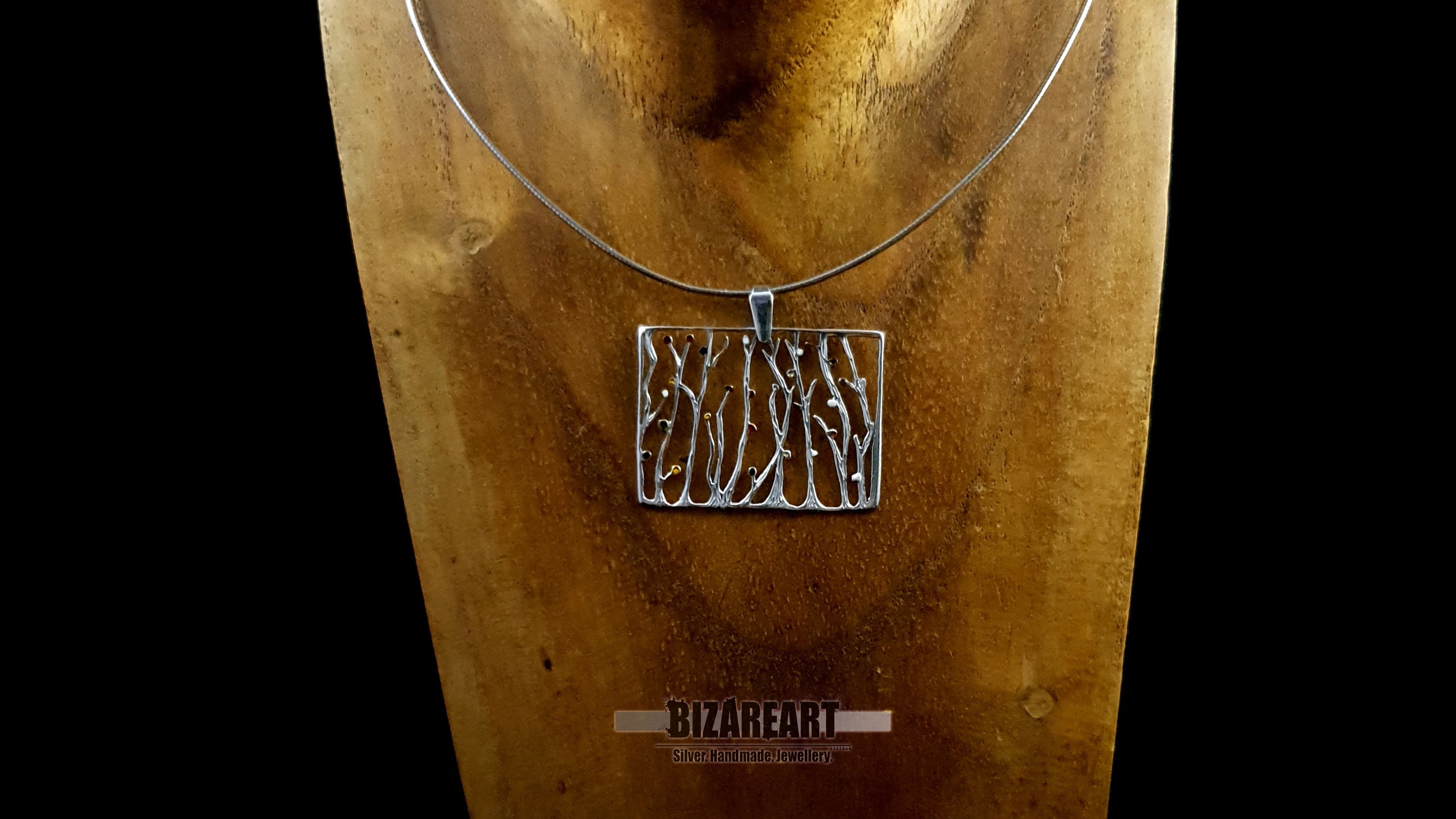 A detailed close-up shot of the silver seaweed pendant hanging from a chain on a wooden display bust, showcasing how the necklace sits when worn.