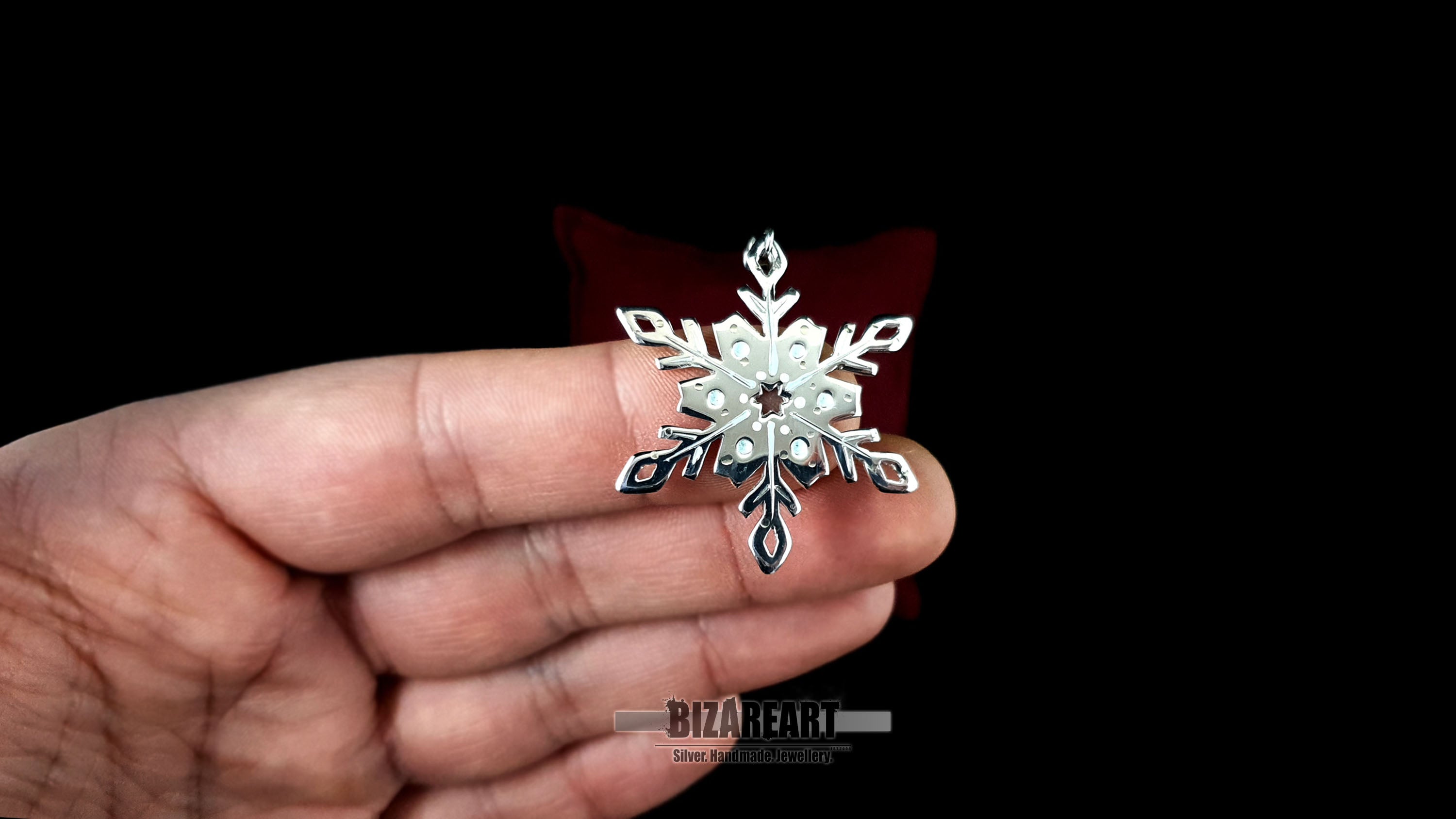 A person holding the snowflake pendant between their fingers to provide a scale reference, showcasing the 4.8 cm height and the shimmering 3D texture of the enamel droplets.