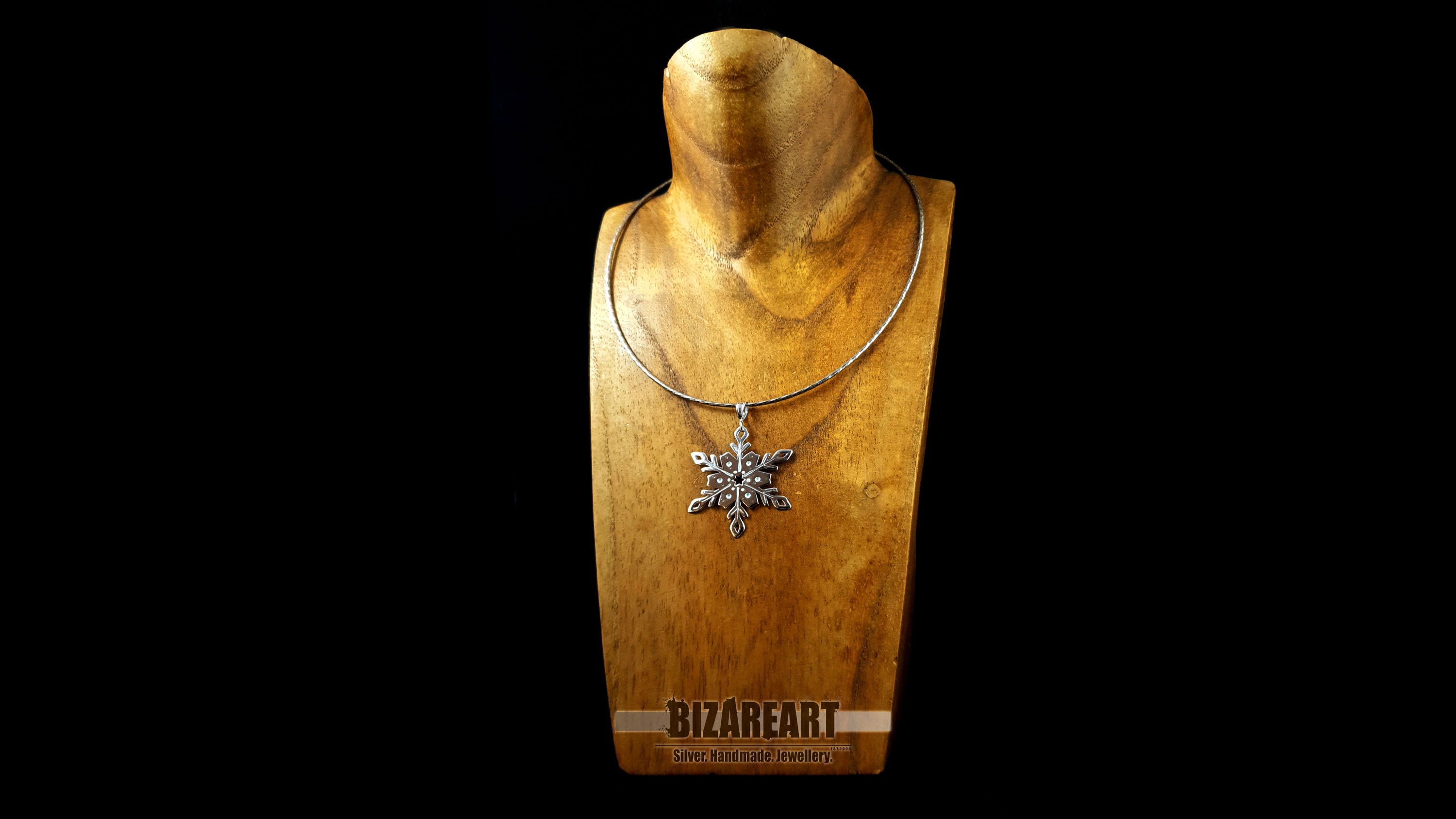 The silver snowflake pendant styled on a silver chain and displayed on a gold-toned jewelry bust to demonstrate how the piece sits when worn.
